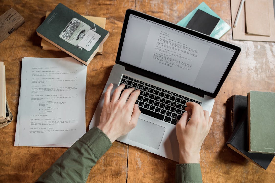 Hands typing on a laptop keyboard surrounded by books and papers