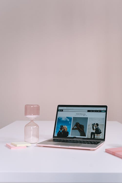 Minimalist workspace with a laptop and pink hourglass representing lost time
